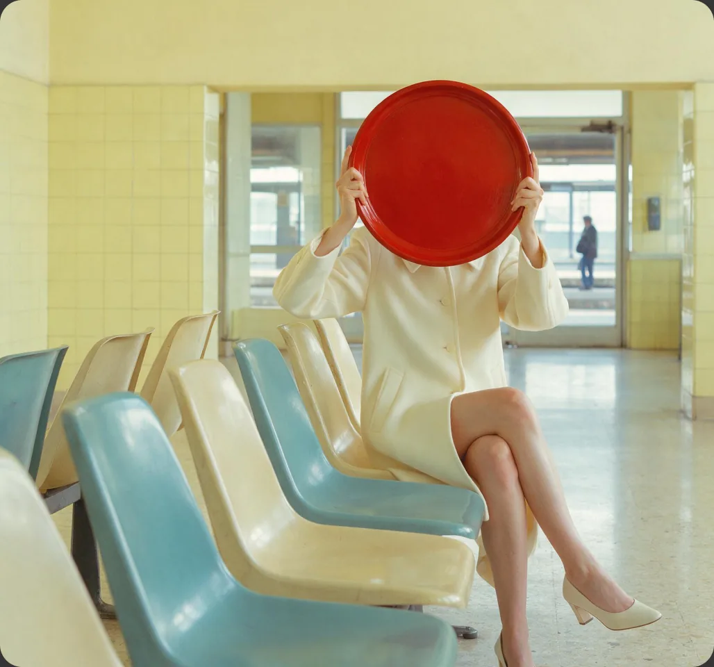 A person holding a bright red circle in a stylized waiting-room scene from Pika